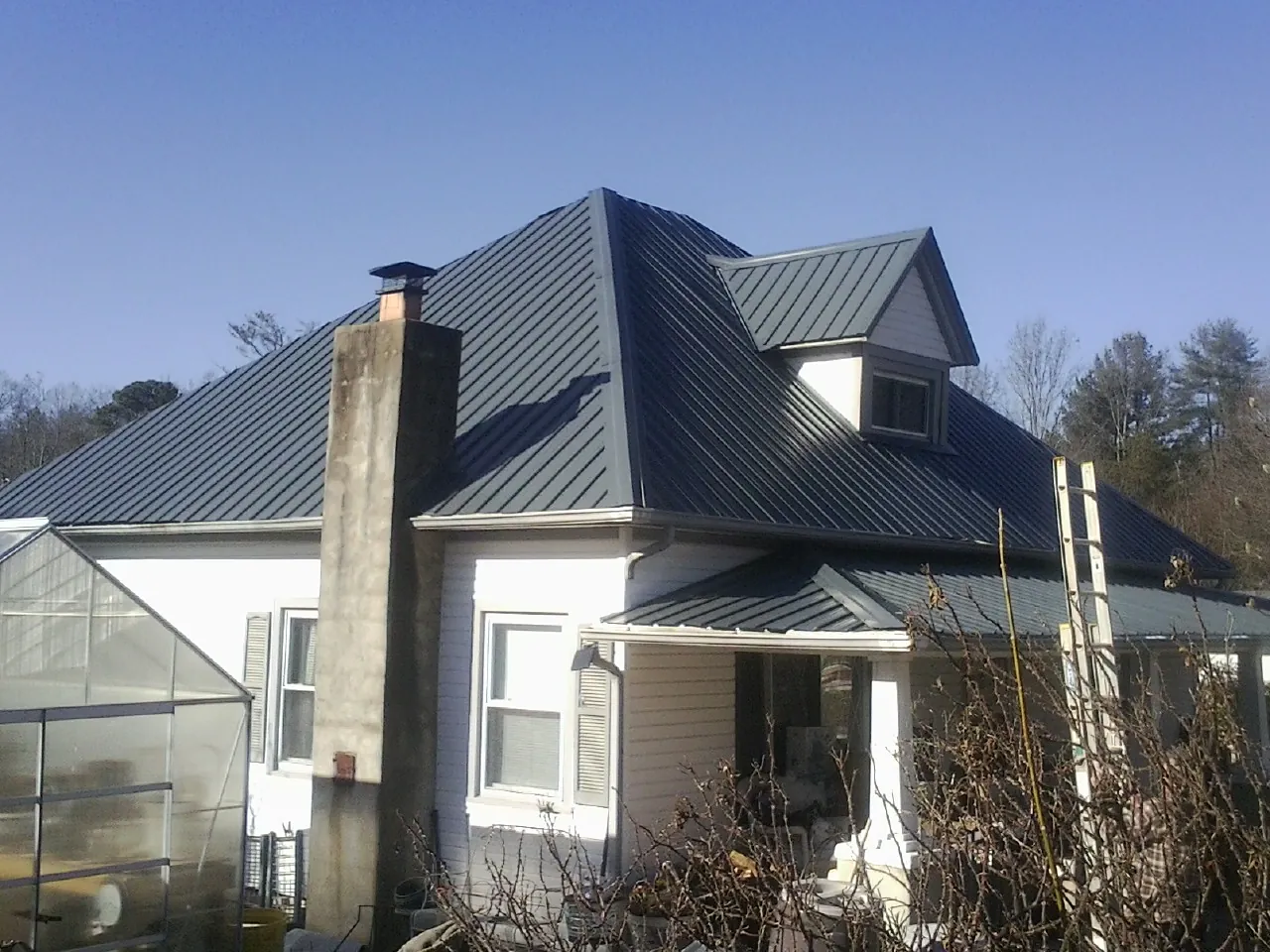 Dark blue standing seam metal roof on a white farmhouse with dormer — Slate & Tile Roof Repair by Roofing Brothers in Jamesville