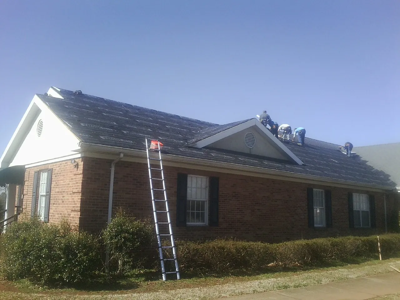 Crew tearing shingles off a brick ranch roof with a ladder set — Emergency Roof Repair work by our crew in Jamesville