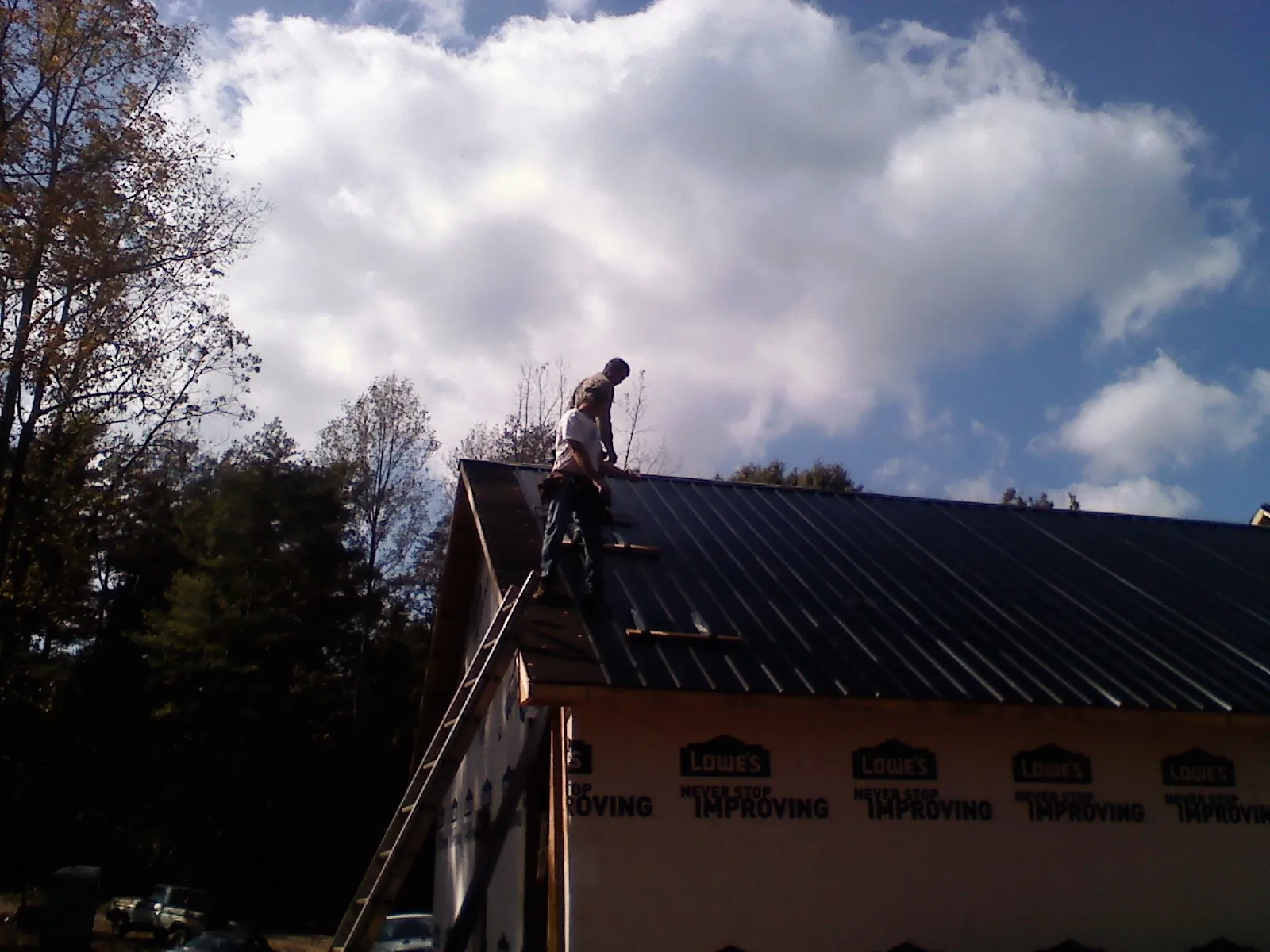 Roofer fastening dark metal panels high against a cloudy sky, from a Roof Inspection job in Jamesville