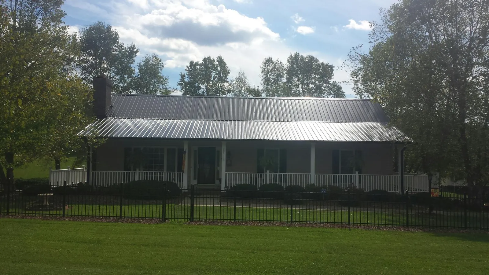 Gray metal roof on a brick ranch with a full width front porch — Gutter Guard Installation work by our crew in Jamesville